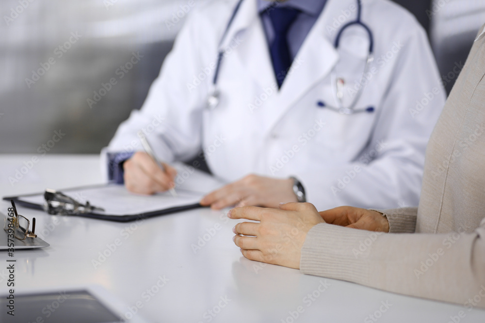 Unknown male doctor and patient woman discussing something while sitting in clinic and using clipboard. Best medical service in hospital, medicine, pandemic stop Unknown male doctor and patient woman discussing something while sitting in clinic and using clipboard. Best medical service in hospital, medicine, pandemic stop