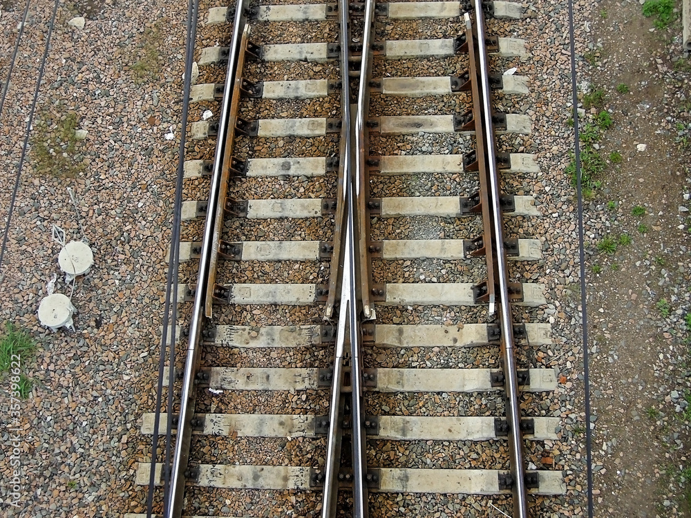 Fototapeta premium View from above onto railroad ways crossing between themselves. Tracks consist of steel rails, installed on ties (sleepers) & ballast, on which rolling stock, usually fitted with metal wheels, moves
