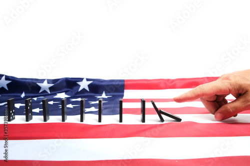 White man's finger pushing a Domino causing a chain reaction against background of the us flag.