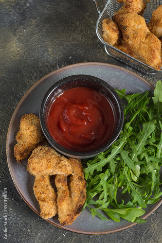 Chicken nuggets on a plate with herbs and tomato sauce and in a deep-frying basket vertical arrangement