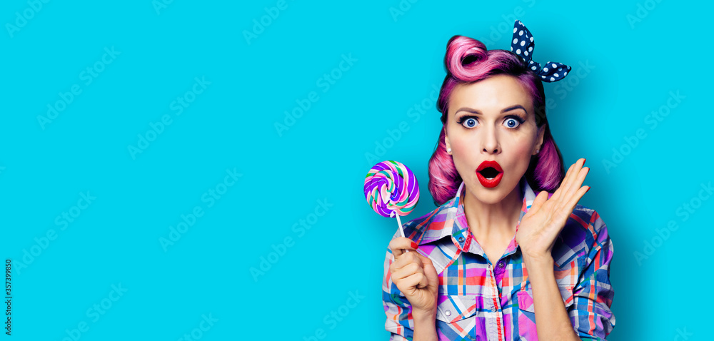 Purple head excited surprised woman with lollipop. Pinup girl with opened mouth. Beauty model at retro fashion and vintage concept. Aqua blue color background with copy space for some advertise text.