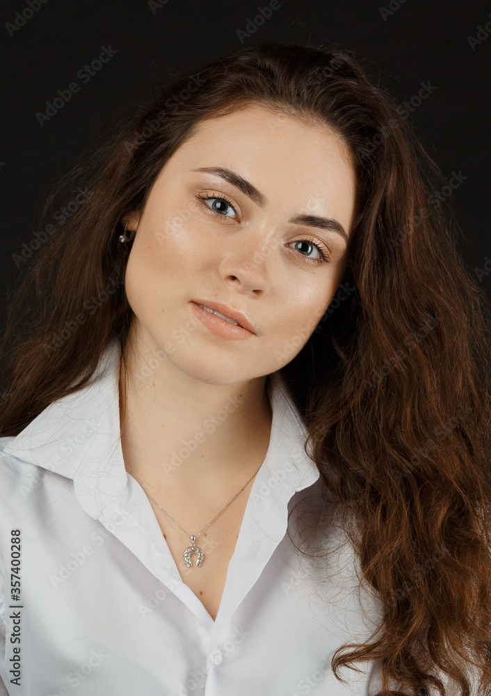 Portrait of a beautiful young woman with dark hair in a white shirt on a dark background Portrait of a beautiful young woman with dark hair in a white shirt on a dark background