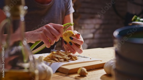 Woman peeling ginger and vegetables for cooking on kitchen table. Closeup hands. Cosy dark room. Real, authentic cooking. 