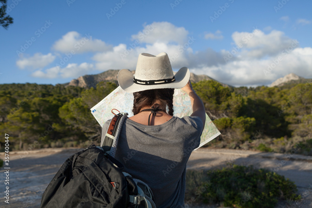 A woman hiking in the mountains of Majorca. A hiker looking at the map while traveling on the island of majorca. The girl is wearing a hat and an Australian look, has long hair and two braids. A woman hiking in the mountains of Majorca. A hiker looking at the map while traveling on the island of majorca. The girl is wearing a hat and an Australian look, has long hair and two braids.