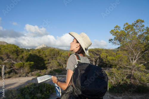 A woman hiking in the mountains of Majorca. A hiker looking at the map while traveling on the island of majorca. The girl is wearing a hat and an Australian look, has long hair and two braids.