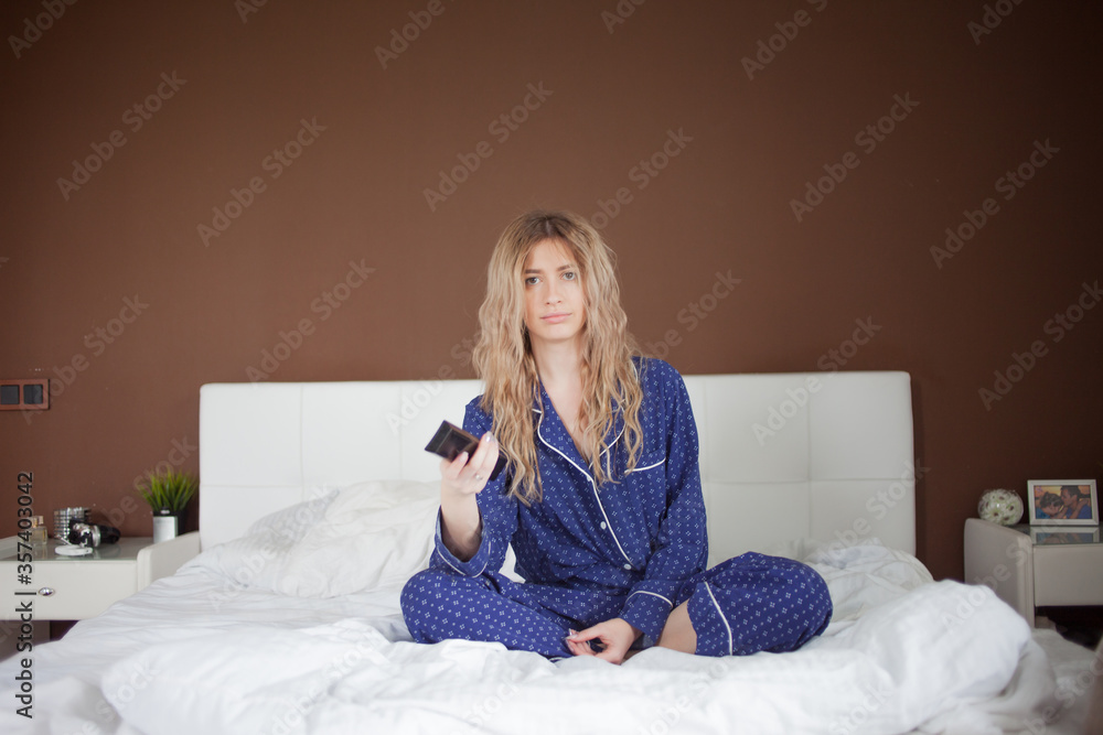 young tired woman in blue pajamas is sitting in bed watching TV young tired woman in blue pajamas is sitting in bed watching TV