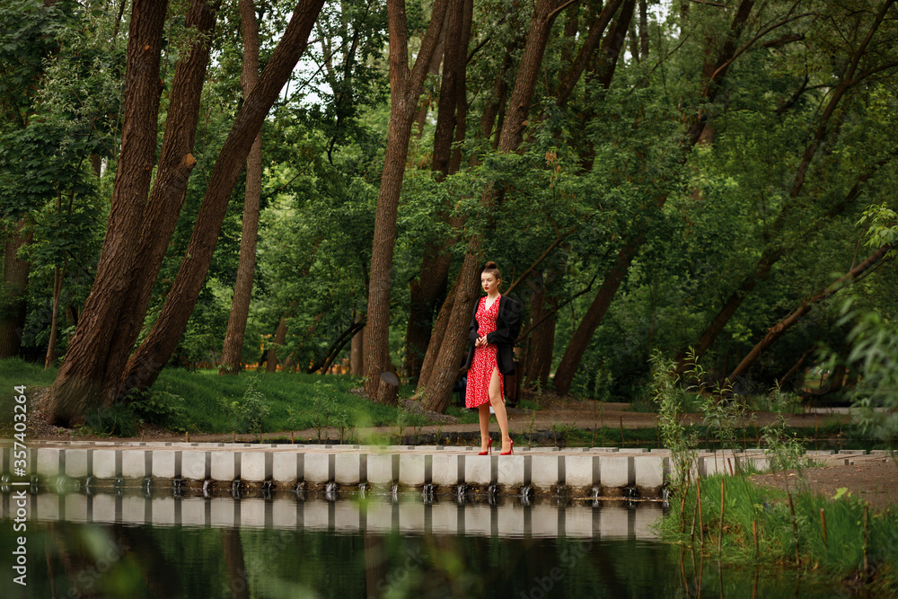 Fototapeta premium A girl walks in a beautiful city park in the summer. walk after the rain. red dress, red shoes