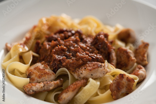 fettuccine pasta with fried chicken and sun-dried tomatoes in white bowl closeup