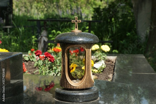 one large lamp with a cross stands on a black marble slab of a grave in a cemetery