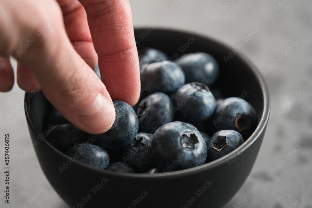 Man hand pick ripe blueberries from black bowl on concrete background closeup Man hand pick ripe blueberries from black bowl on concrete background closeup