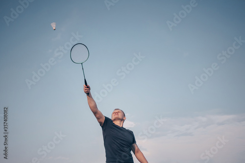 Young Caucasian man plays badminton on a background of blue sky. The concept of an amateur game of badminton, outdoor activities. Copyspace, bottom view.. © Ольга Холявина