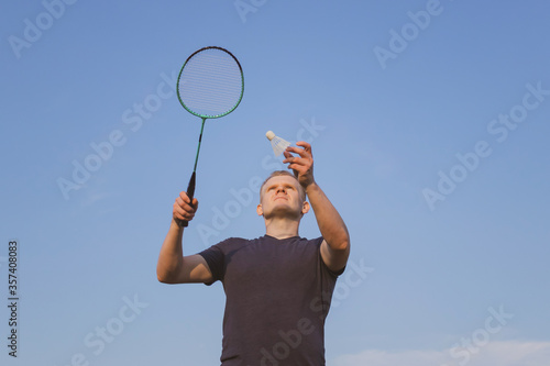 Young Caucasian man plays badminton on a background of blue sky. The concept of an amateur game of badminton, outdoor activities. Copyspace, bottom view. © Ольга Холявина