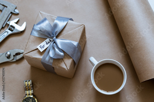 gift in craft packaging with a cup of coffee, a watch and accessories for repairs on the table for Father's Day