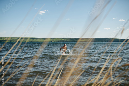 Man running in lake water towards the shore. Shot thrugh dry grass spikes photo