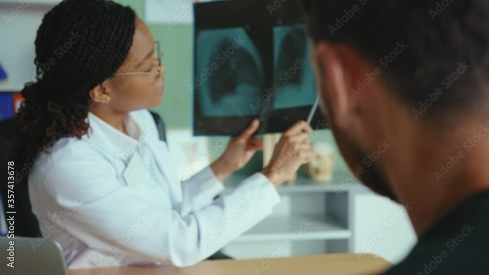 Female african american doctor showing x-ray scan of lungs to the patient, explaining the diagnosis and giving instructions for healing. Medical, health care concept. Female african american doctor showing x-ray scan of lungs to the patient, explaining the diagnosis and giving instructions for healing. Medical, health care concept.