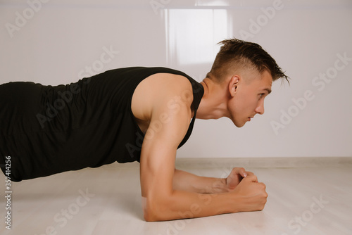 Young man in sport stylish clothes standing in plank pose or doing horizontal push-up in living room at home.
