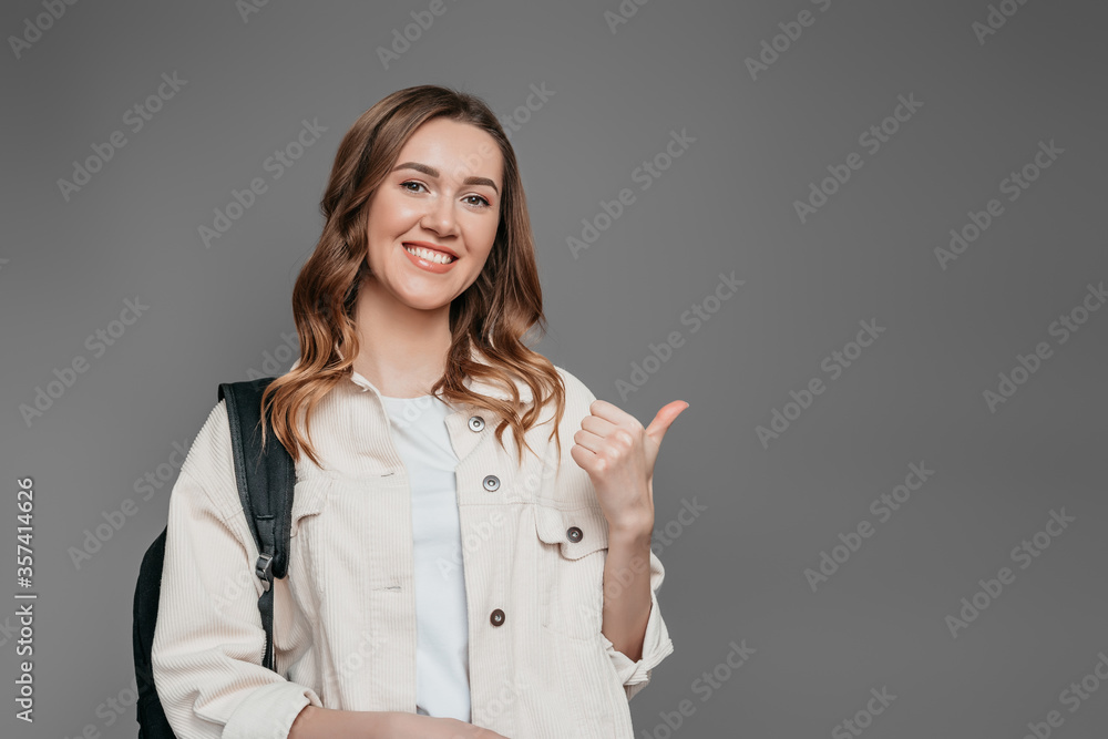 Portrait of student girl with backpack pointing finger to copy space isolated over grey wall background, copy space Portrait of student girl with backpack pointing finger to copy space isolated over grey wall background, copy space