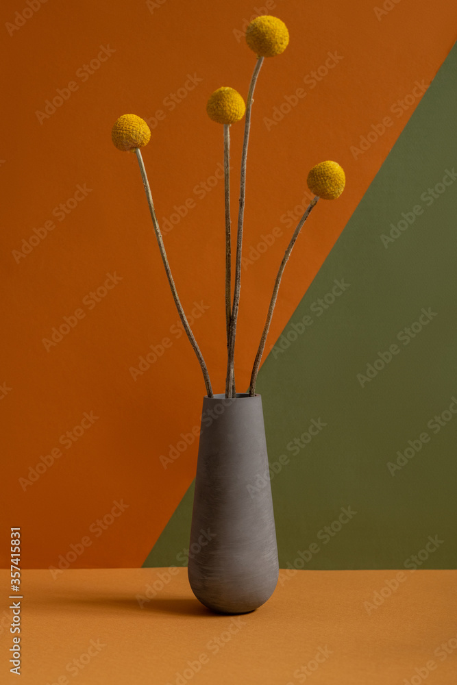 Grey clay jug or vase with several yellow dried wildflowers with long stems Grey clay jug or vase with several yellow dried wildflowers with long stems