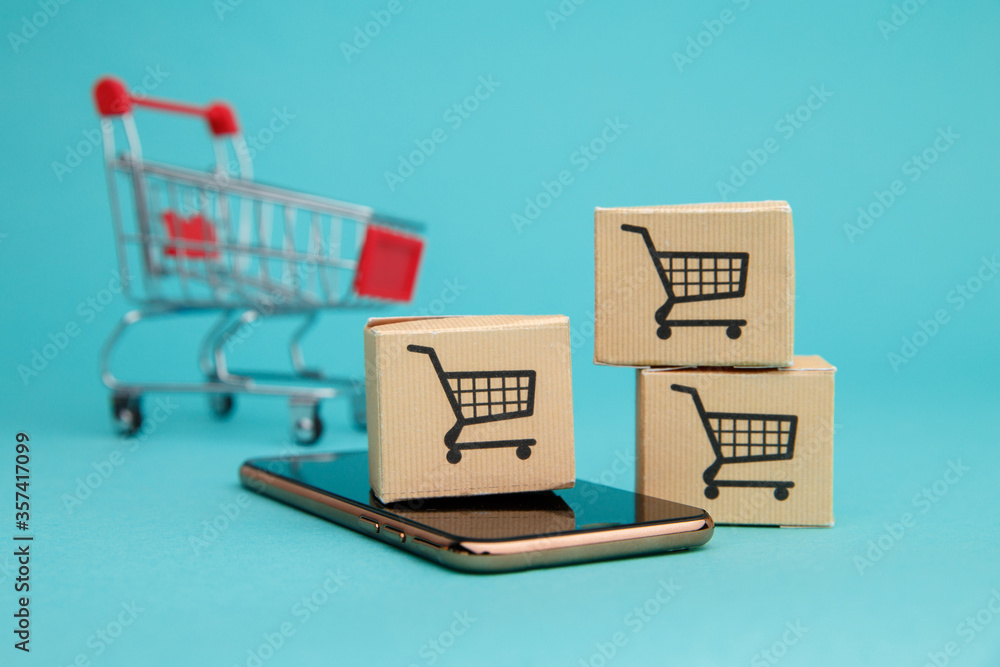 Concept of online Shopping. Boxes and shopping cart above smartphone isolated on blue background.