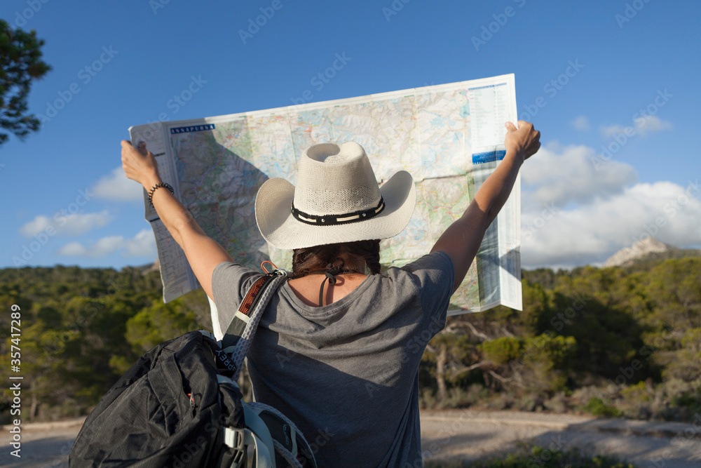 A woman hiking in the mountains of Majorca. A hiker looking at the map while traveling on the island of majorca. The girl is wearing a hat and an Australian look, has long hair and two braids.