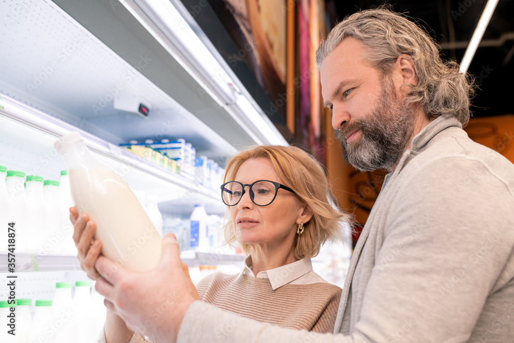 Aged serious bearded man and his blond wife choosing milk on display