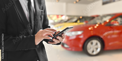 Businessman using smartphone on blurred background of new car displayed in showroom dealer with copy space.