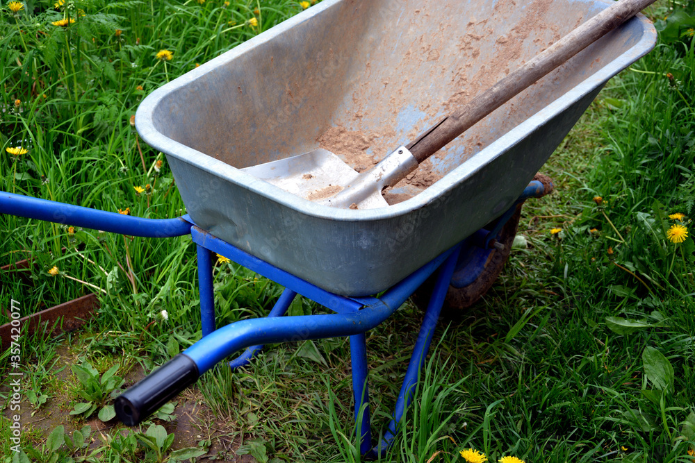 Garden cart and scoop close-up. A device for transporting cargo-sand, clay, peat, humus, earth. Yard equipment on wheels for the garden, garden and dacha. Garden cart and scoop close-up. A device for transporting cargo-sand, clay, peat, humus, earth. Yard equipment on wheels for the garden, garden and dacha.