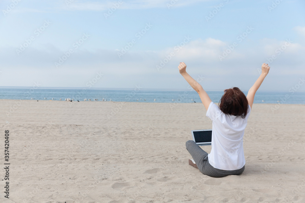 Happy freelance woman raised her hands up while sitting on the empty beach / sand with laptop. Happy freelance woman raised her hands up while sitting on the empty beach / sand with laptop.