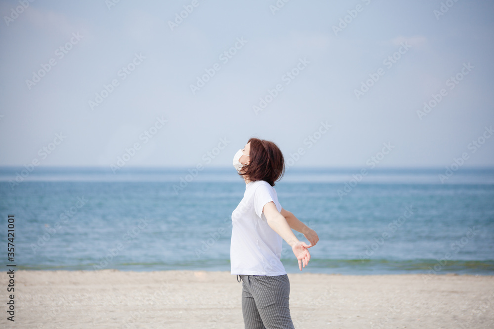 Young pretty woman with medical mask on the beach. Tourist woman in medical face mask on beach.