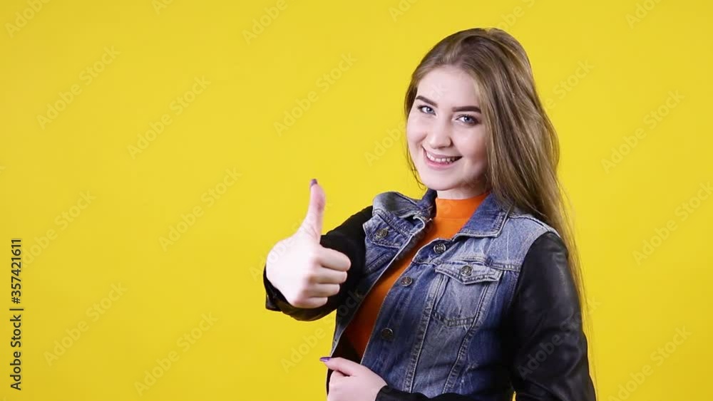 Young positive woman shows a gesture a thumb up, on a yellow background. Girl shows two hands thumbs up, class super Young positive woman shows a gesture a thumb up, on a yellow background. Girl shows two hands thumbs up, class super