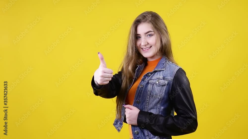 Young positive woman shows a gesture a thumb up, on a yellow background. Girl shows two hands thumbs up, class super Young positive woman shows a gesture a thumb up, on a yellow background. Girl shows two hands thumbs up, class super