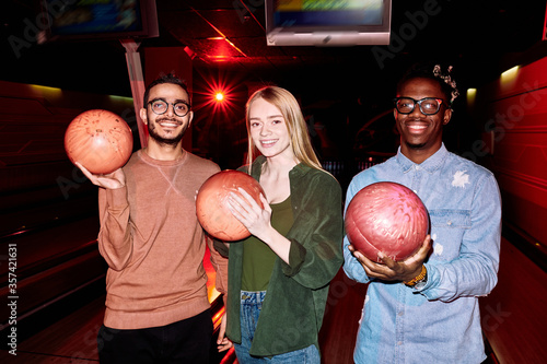 Two young intercultural men and blond Caucasian girl with bowling balls