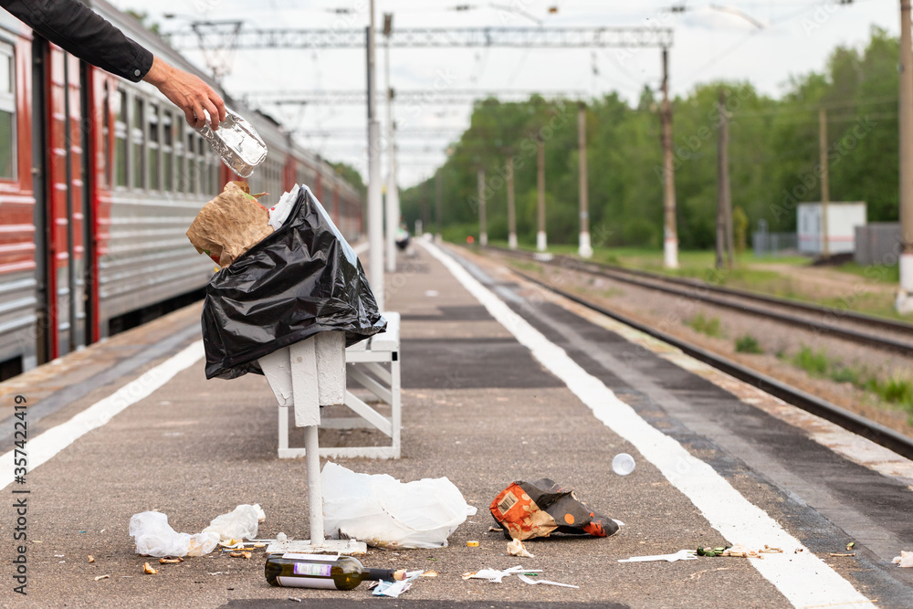 Hand of unknown man throws trash into overcrowded trash basket on a