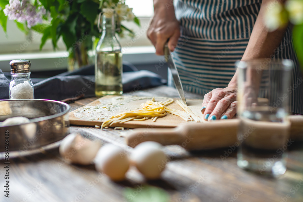 Woman is cutting raw dough with a knife to make homemade noodles. Concept of process of cooking handmade pasta Woman is cutting raw dough with a knife to make homemade noodles. Concept of process of cooking handmade pasta