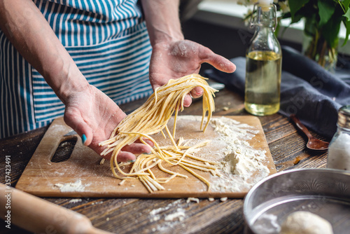 Woman is carefully holding raw homemade noodles in her hands. Process of cooking handmade pasta in a cozy atmosphere