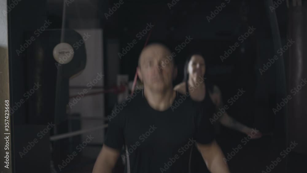 Front view of smiling man jumping rope with blurred happy woman exercising at the background. Portrait of joyful healthy people training in fitness club. Sport, lifestyle, enjoyment. Front view of smiling man jumping rope with blurred happy woman exercising at the background. Portrait of joyful healthy people training in fitness club. Sport, lifestyle, enjoyment.