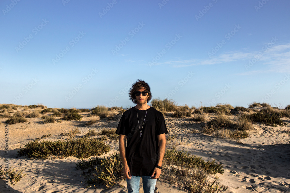Modelo masculino con gafas de sol y camiseta negra en la playa