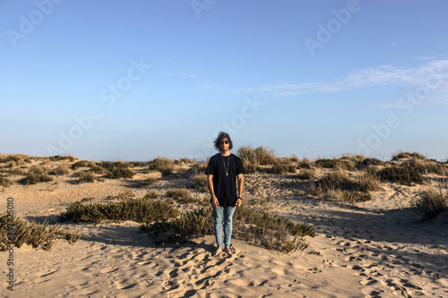 Modelo masculino con gafas de sol y camiseta negra en la playa