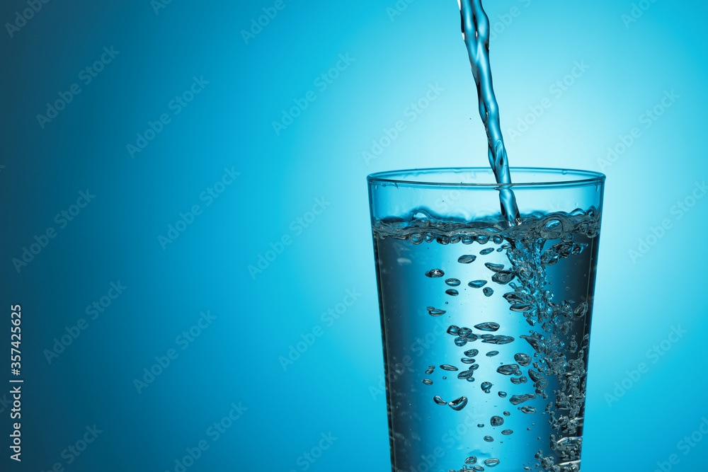 Fresh water pours into a glass on a blue background. Fresh water pours into a glass on a blue background.