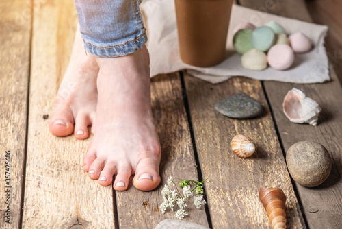 Cared female feet on a background of old boards in the village style with shells, stones. Concept of summer pedicure, recreation and travel. photo