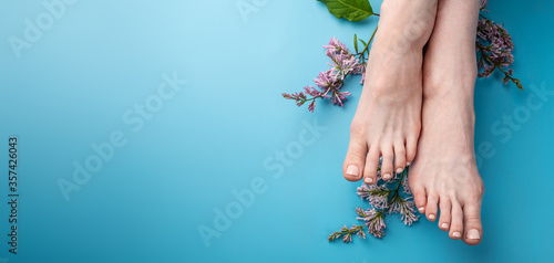 Beautiful women's feet with beige nail polish on a blue background with lilac flowers. Concept of foot care, summer pedicure. Top view and copy space photo