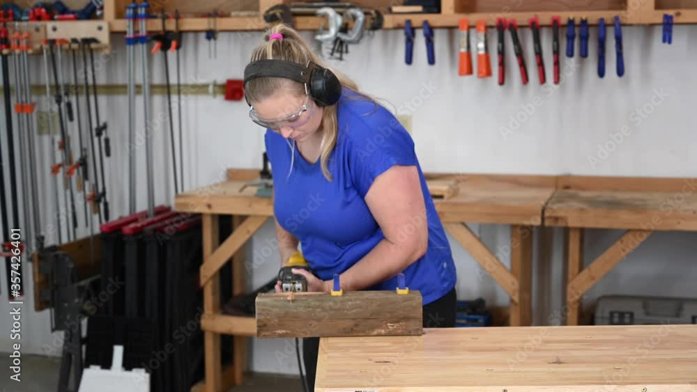 Female young adult woodworking cutting a plank with a hand electric sawsall. Female young adult woodworking cutting a plank with a hand electric sawsall.