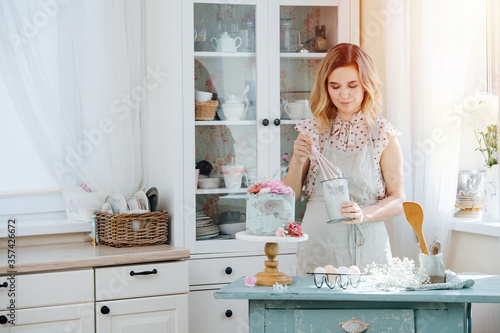 Focused happy housewife with beautiful hair whipping cream for a cake
