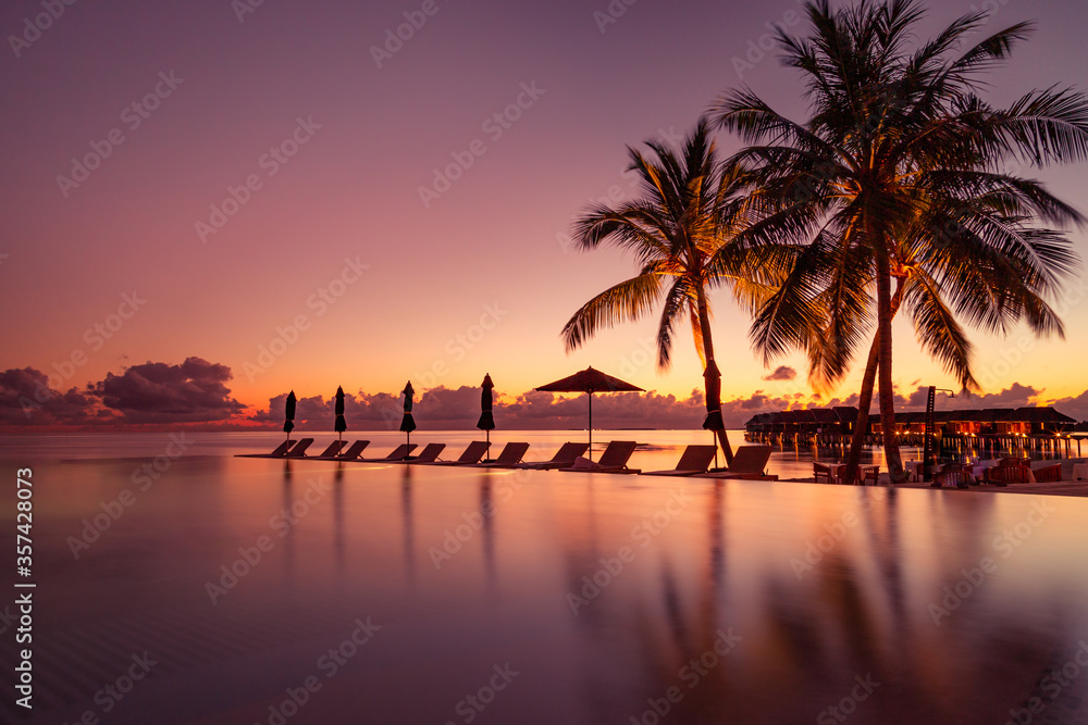 Beautiful poolside and sunset sky. Luxurious tropical beach landscape, deck chairs and loungers and water reflection. Outdoor tourism landscape. Luxurious beach resort. Summer travel and vacation
