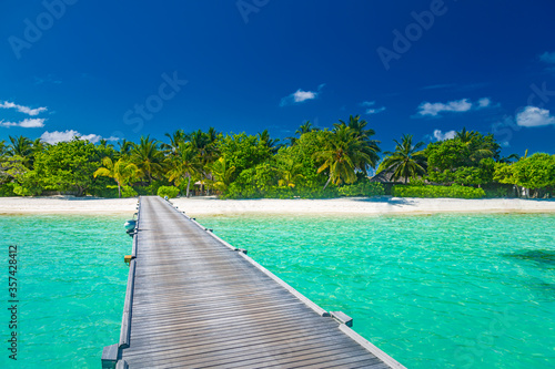 Exotic island paradise. Travel, tourism or vacations concept. Tropical beach resort, long jetty with palm trees over white sand, blue sky. Luxury summer holiday vacation landscape
