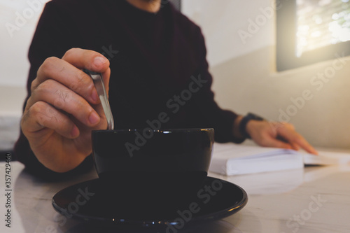 Tableau sur toile Close up image of a man stirring a coffee cup and reading a book in a cafe