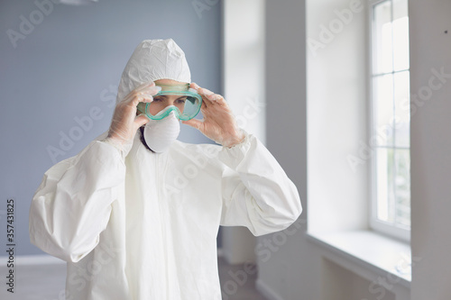 Male medicine specialist wearing PPE face mask and body protective suit putting on protection glasses