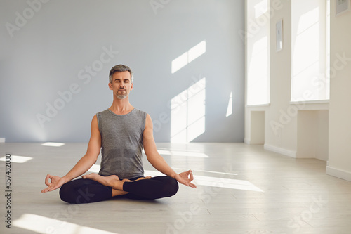 Fototapeta Naklejka Na Ścianę i Meble -  Yoga man. Bearded guy is practicing yoga in a lotus position sitting in a studio