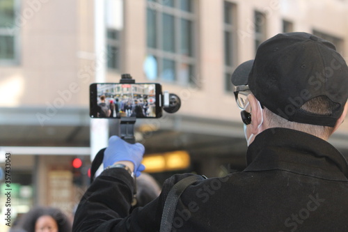 Sydney, NSW / Australia - 6/6/2020: Black Lives Matter. Man taking video of the demonstrators, recording with his phone on a gimbal. He is wearing blue disposable gloves. During a pandemic of Covid 19