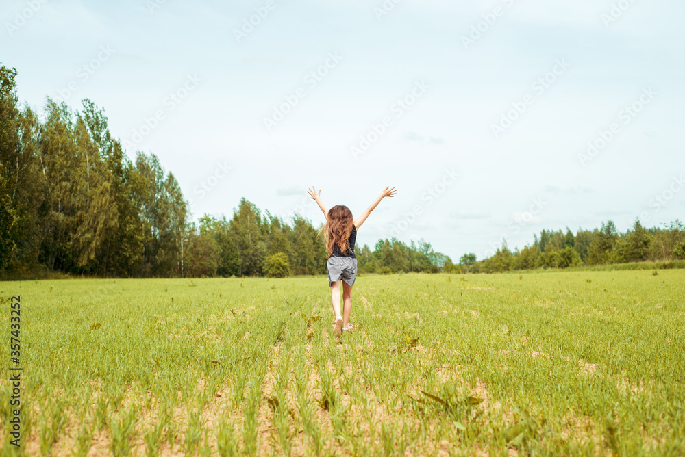 Little girl running on a meadow in a field of flowers, Summer day. barefoot jumping on the grass, happy laughs. Horizon and sky.freshness idea and freedom. happy childhood